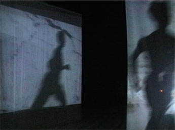 dancer running past screens with projected video & shadow reflected in large mirror